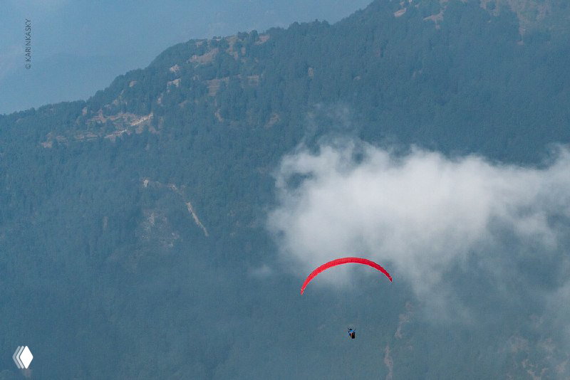 Одинокий параплан в облаке на фоне горного склона; тонкая дымка и контраст крыла на фоне рельефа.