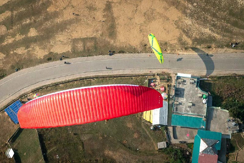 Вид сверху на красное крыло и сельский ландшафт у подножия горы; дороги и дома внизу подчёркивают высоту полёта.