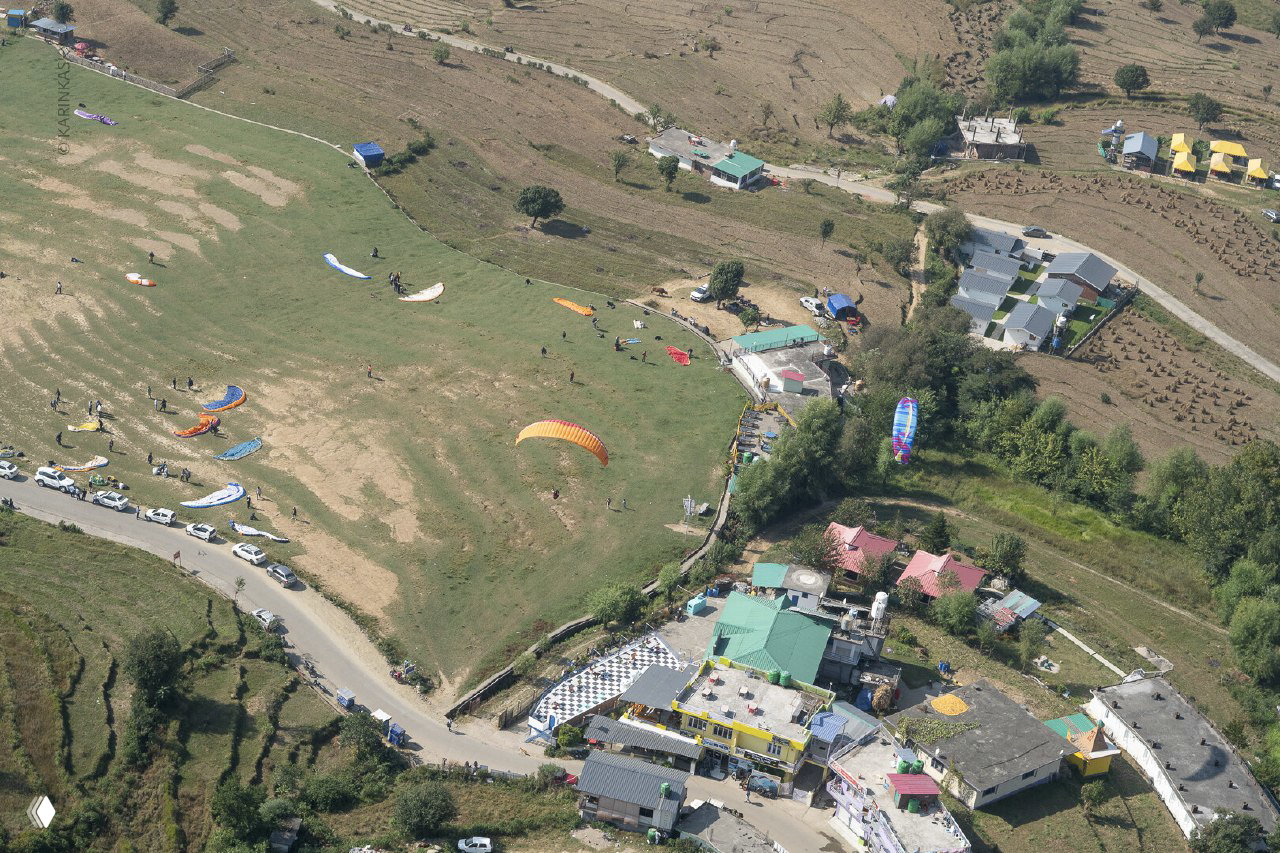 Аэрофотосъёмка посадочной поляны в Бире: расставленные парапланы, машины и инфраструктура рядом с площадкой для приземлений.
