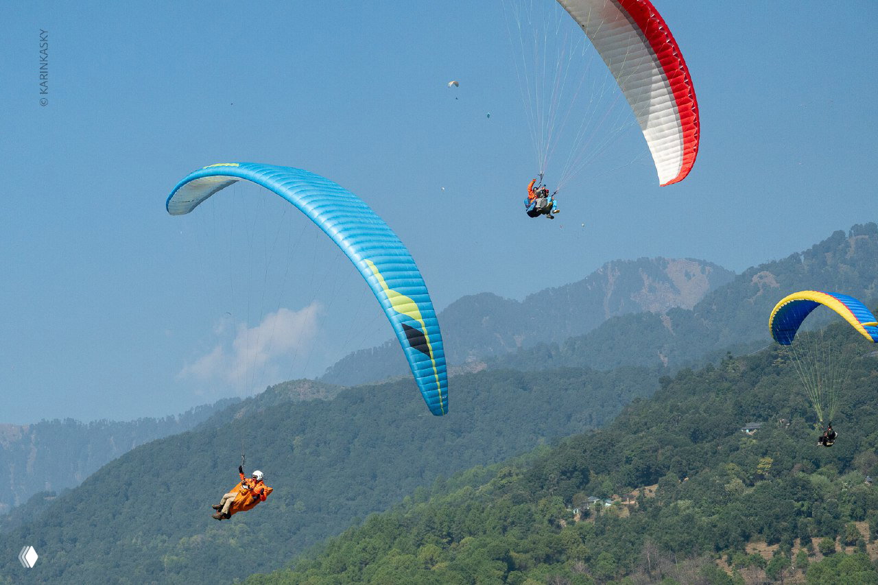 Парапланист тандемом на фоне гор и чистого неба; кадр подчёркивает моменты приближения к посадке и необходимость внимательности.