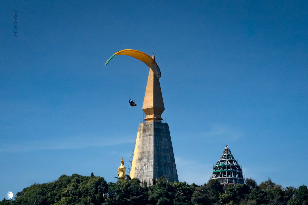 Парапланист выполняет пролёты рядом с архитектурной достопримечательностью и статуей Будды — воздушный кадр с гонок в Таиланде.