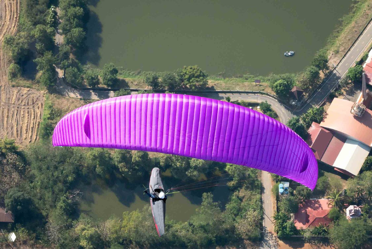 Фиолетовый параплан крупным планом над участком с водоёмом и домами — воздушная фотография с соревнований в Таиланде.