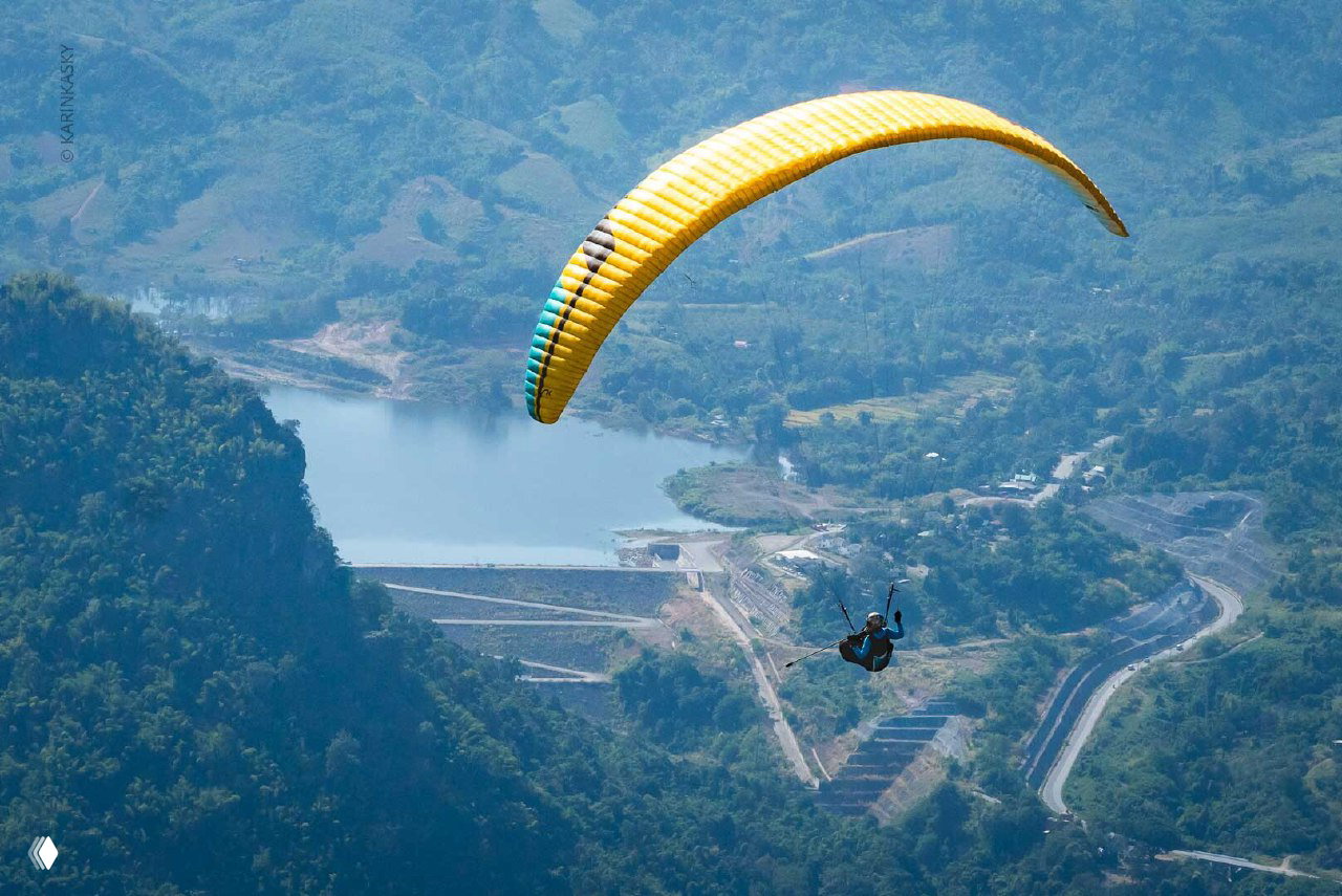 Жёлтый купол параплана в полёте над долиной и водохранилищем, пилот снизу видно снижением и перспективой высоты.