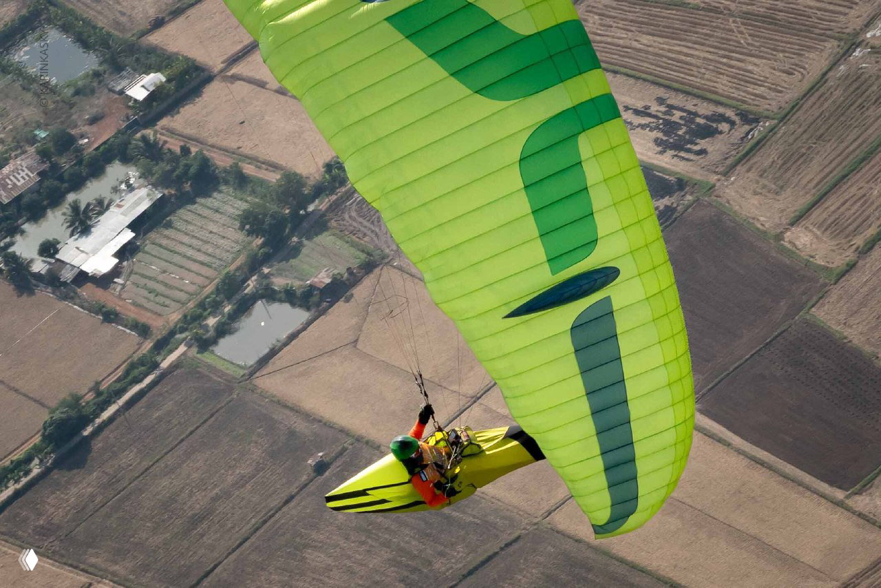 Ярко-зелёный купол и пилот в гоночном подвесе на фоне расчистки полей и сельской местности — ощущение скорости и высоты.