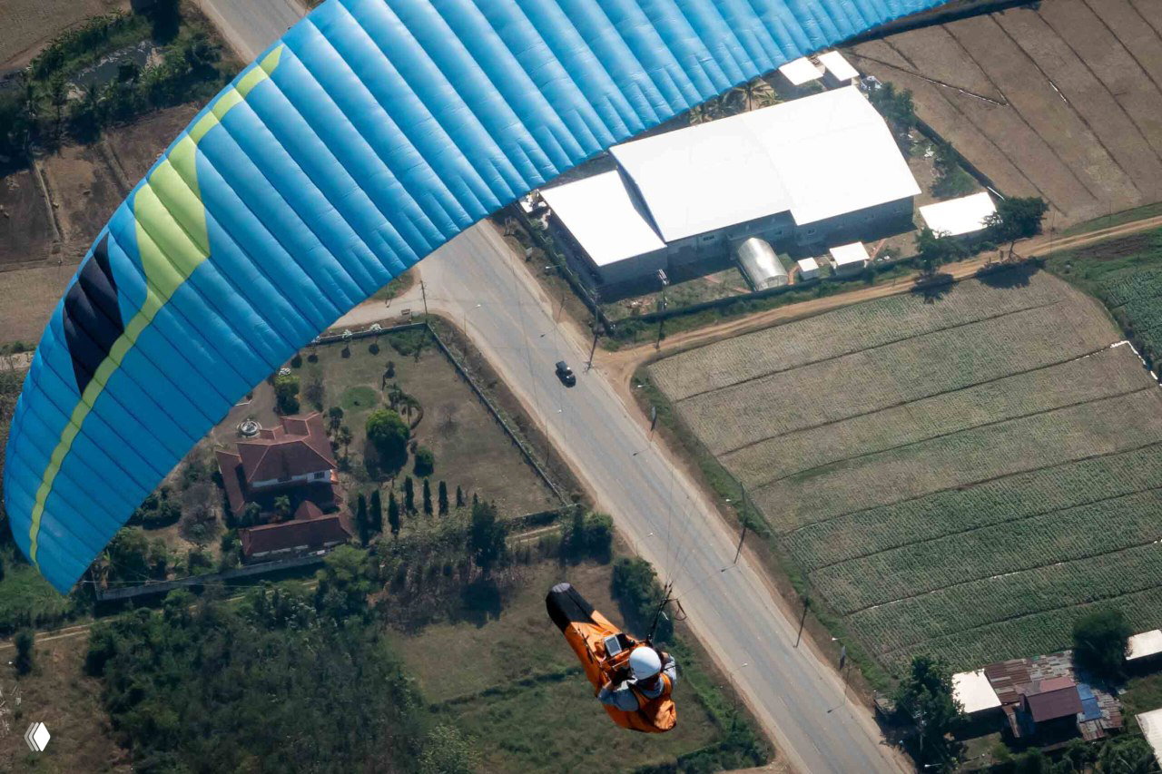 Синий купол над дорогой и домами, пилот в подвесе над трассой; снимок подчёркивает маршрутный профиль и окружающую инфраструктуру.