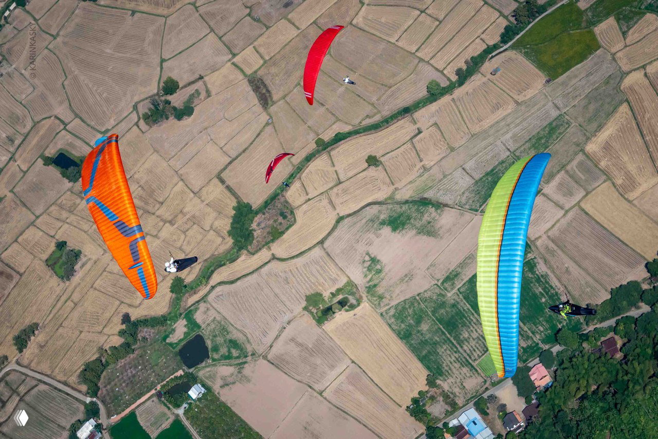 Группа разноцветных парапланов над сельскохозяйственными участками Таиланда, командная сцена соревнований и учебные полёты рядом с трассой