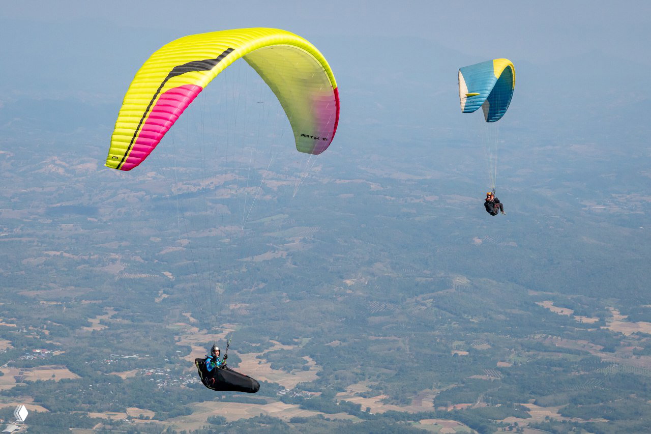 Несколько пилотов на парапланах в небе над холмами и долинами, яркие крылья на фоне пространного ландшафта Том Yum Cup 2024
