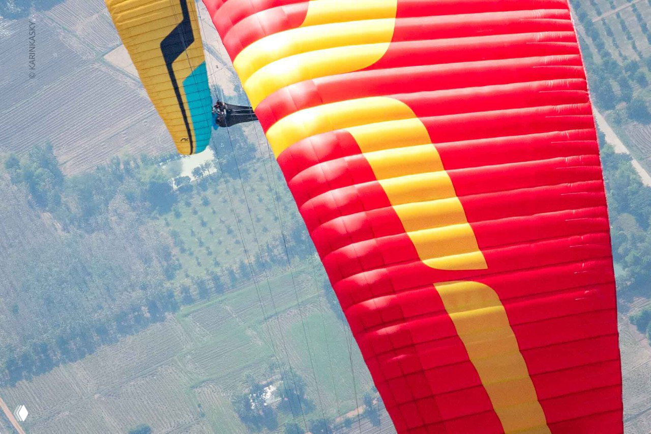 Крупный план ярко-красного крыла параплана, вид снизу и фрагмент второго крыла — демонстрация форм и цвета оборудования в соревнованиях