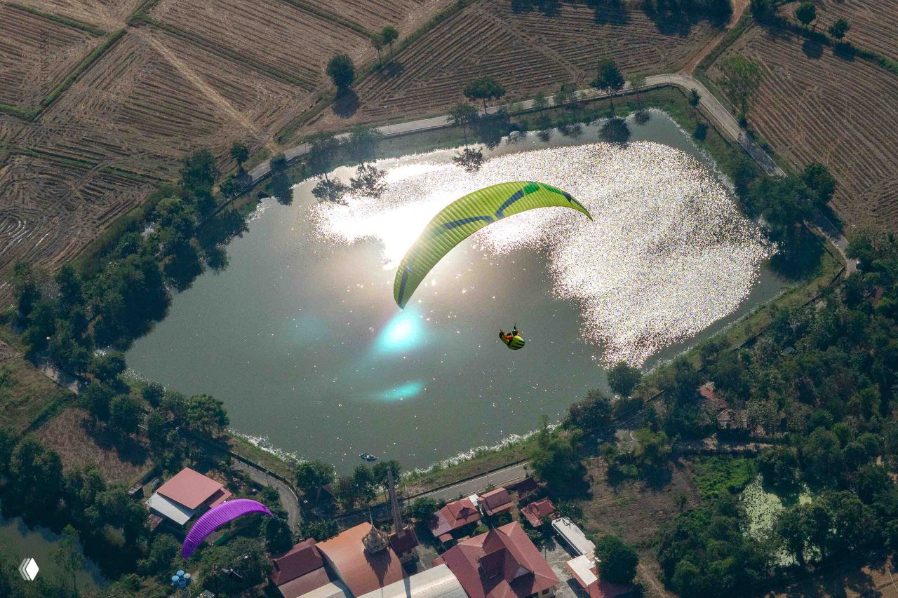 Параплан над зеркальным водоёмом, отражение солнца и ландшафта — живописный кадр с соревнований, демонстрирующий высоту и маршрут