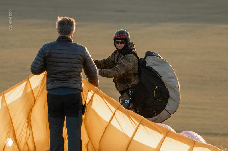 Подготовка к запуску: инструктор и пилот рядом с расправленным крылом на земле, раннее утро на ровной площадке перед полётом.