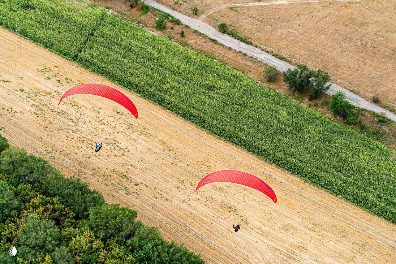 Воздушный снимок двух парапланов над полем и полосами посевов, вид сверху показывает маршруты и возможные зоны посадки.