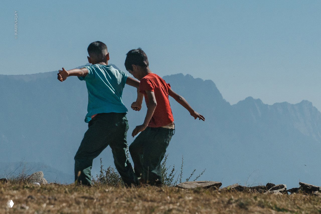Двое мальчиков на переднем плане на краю обрыва, на заднем плане горные силуэты и перспективы для полётов на параплане в горах