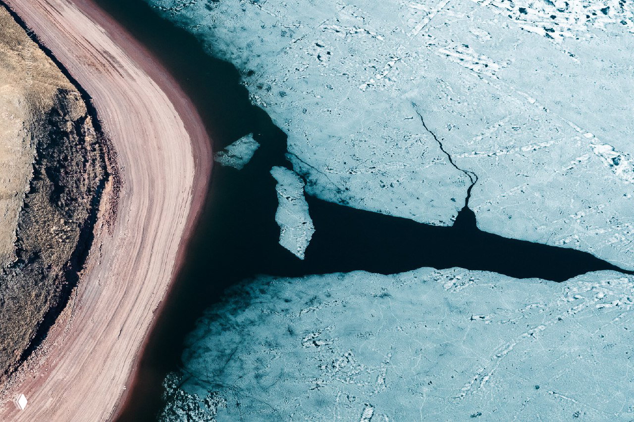 Аэрофотоснимок береговой линии и кромки льда: тёмная вода у берегов, светлые льдины и извилистая полоса суши с текстурами природы.