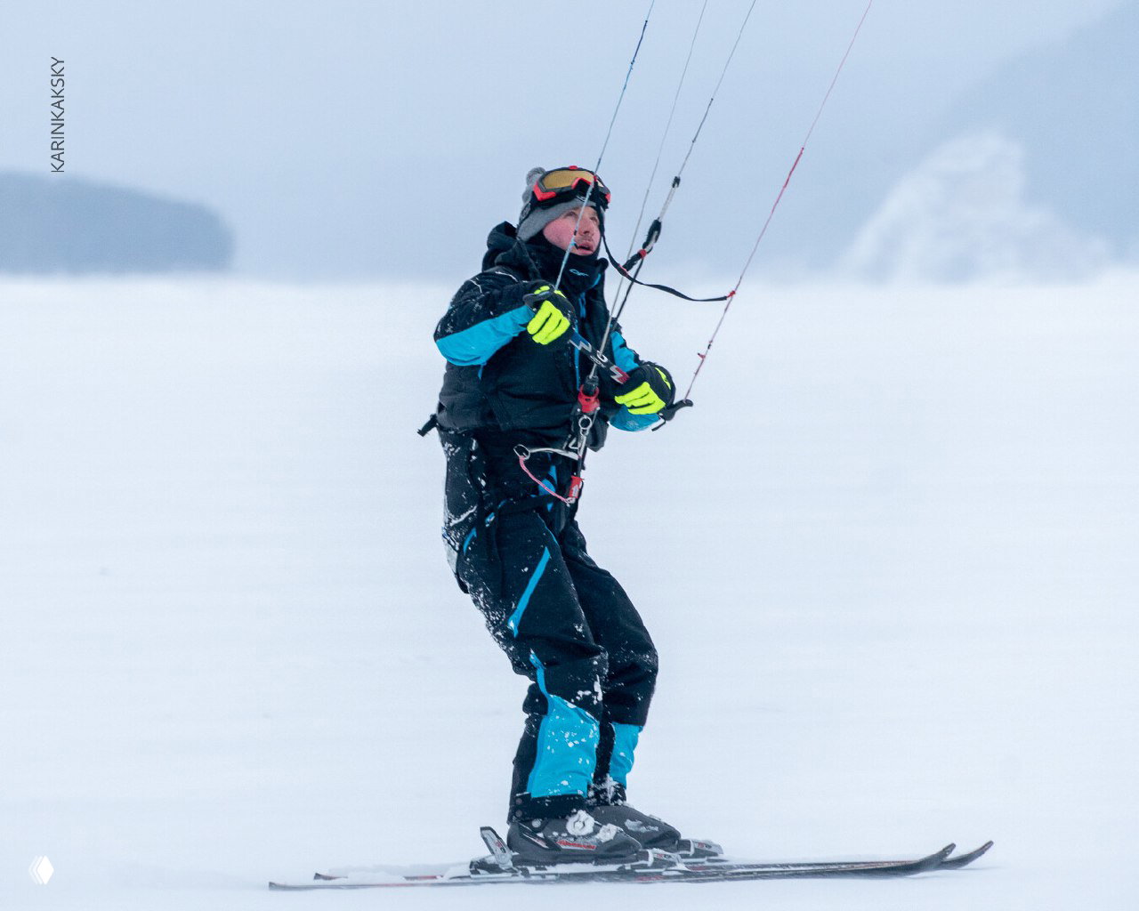Крупный план райдера с кайт-парашютом на Красморе: зимняя экипировка, яркие перчатки, рука на баре управления и снежный туман на фоне.