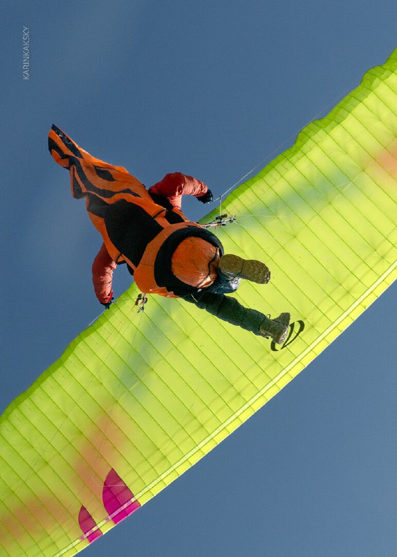 Съемка снизу: пилот на ярко-салатовом крыле в полёте, видны линии и форма параплана в работе на термике.