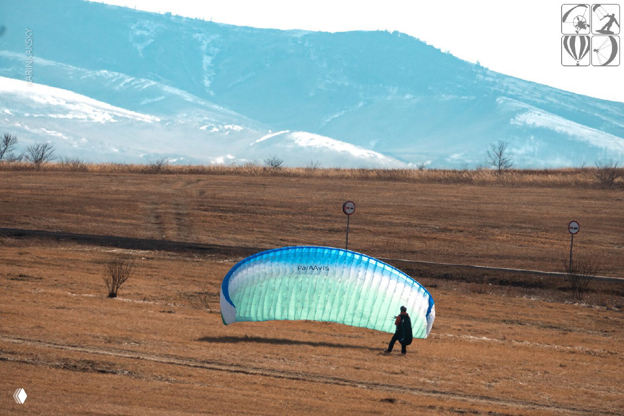 Развернутое крыло параплана на степном поле на фоне гор: отработка старта и работа с крылом в полевых условиях Хакасии.