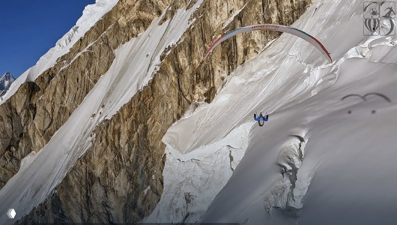 Парапланерист летит рядом с отвесной ледяной стеной и складками ледника; кадр подчёркивает близость к скальным и ледовым породам.