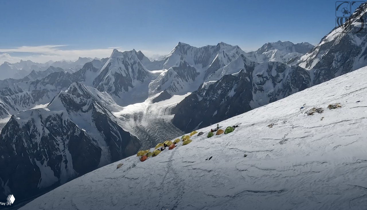 Базовый лагерь с рядами разноцветных палаток на снежном склоне; вокруг — панорама острых ледяных вершин и ледовая долина.