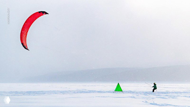 Одинокий кайт в небе над белым льдом Красмора, спортсмен контролирует траекторию на фоне тумана и дальнего заснеженного берега.