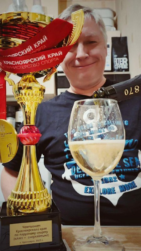 Трофей и бокал победителя крупным планом, на заднем плане улыбающийся Павел Макаров демонстрирует приз Чемпионата Красноярского края по сноукайтингу.