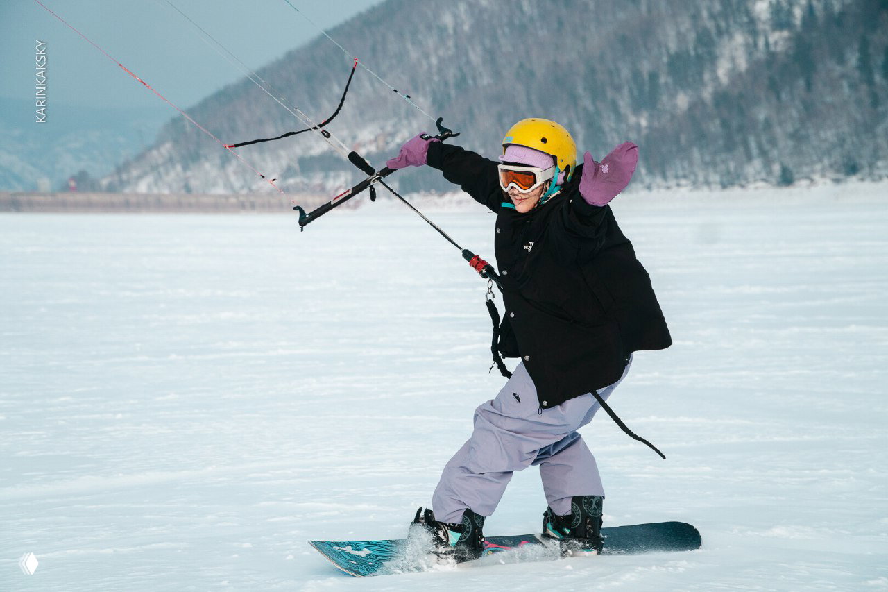 Девушка на сноуборде управляет кайтом в сильный ветер на ровной снежной поверхности, видна энергия и эмоции катания 2 марта.