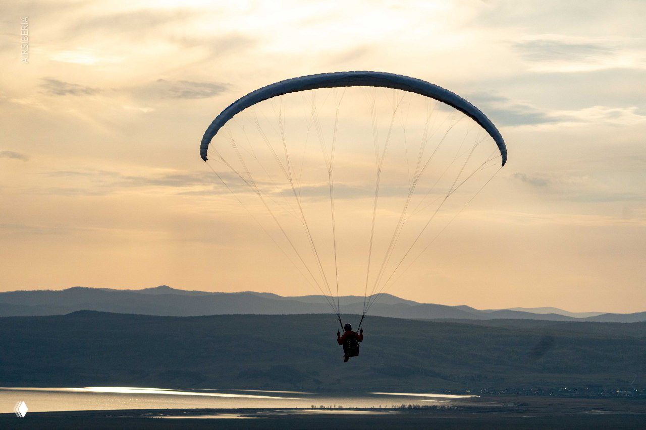 Силуэт парапланиста на фоне заката и водной поверхности водохранилища внизу: спокойная вечерняя сцена полёта.