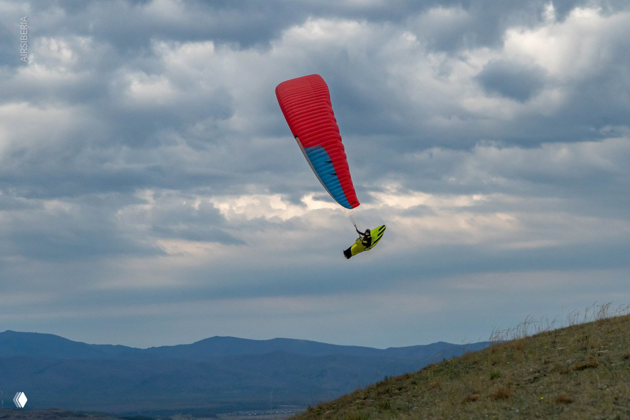 Параплан в небе над холмом и далёким водохранилищем: спокойный полёт на фоне мягкого освещения и рассыпающегося облачного неба.