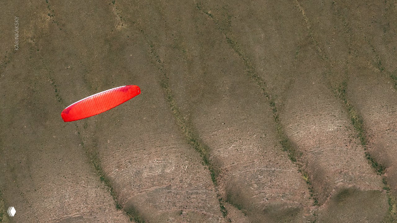 Крупный план красного параплана на фоне текстуры травянистого склона и рельефа — воздушная съёмка, показывающая крыло в полёте над маршрутом.