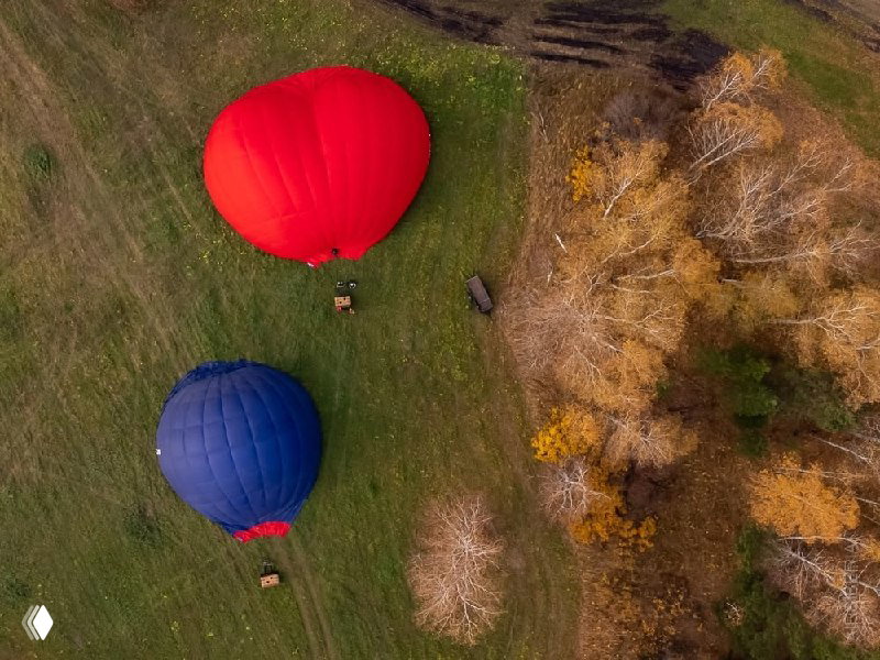 Вид сверху: два шара на земле рядом с берегом/лесным участком — подготовка или посадка, осенние цвета и поля вокруг.