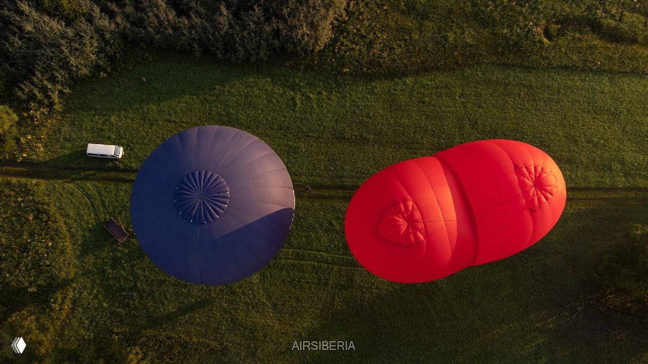 Аэрофотосъёмка сверху: два шара на травяном поле — синие и красные купола, видна геометрия обтекания и следы техники на земле.