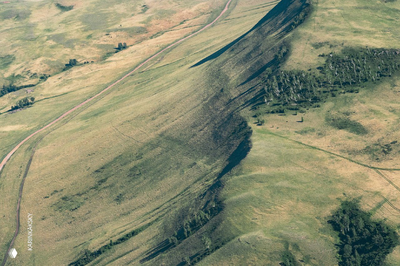 Аэрофотография склона и тени холма с тропинками и зелёным покровом — рельеф для подъёма воздушного потока и приземления параплана.