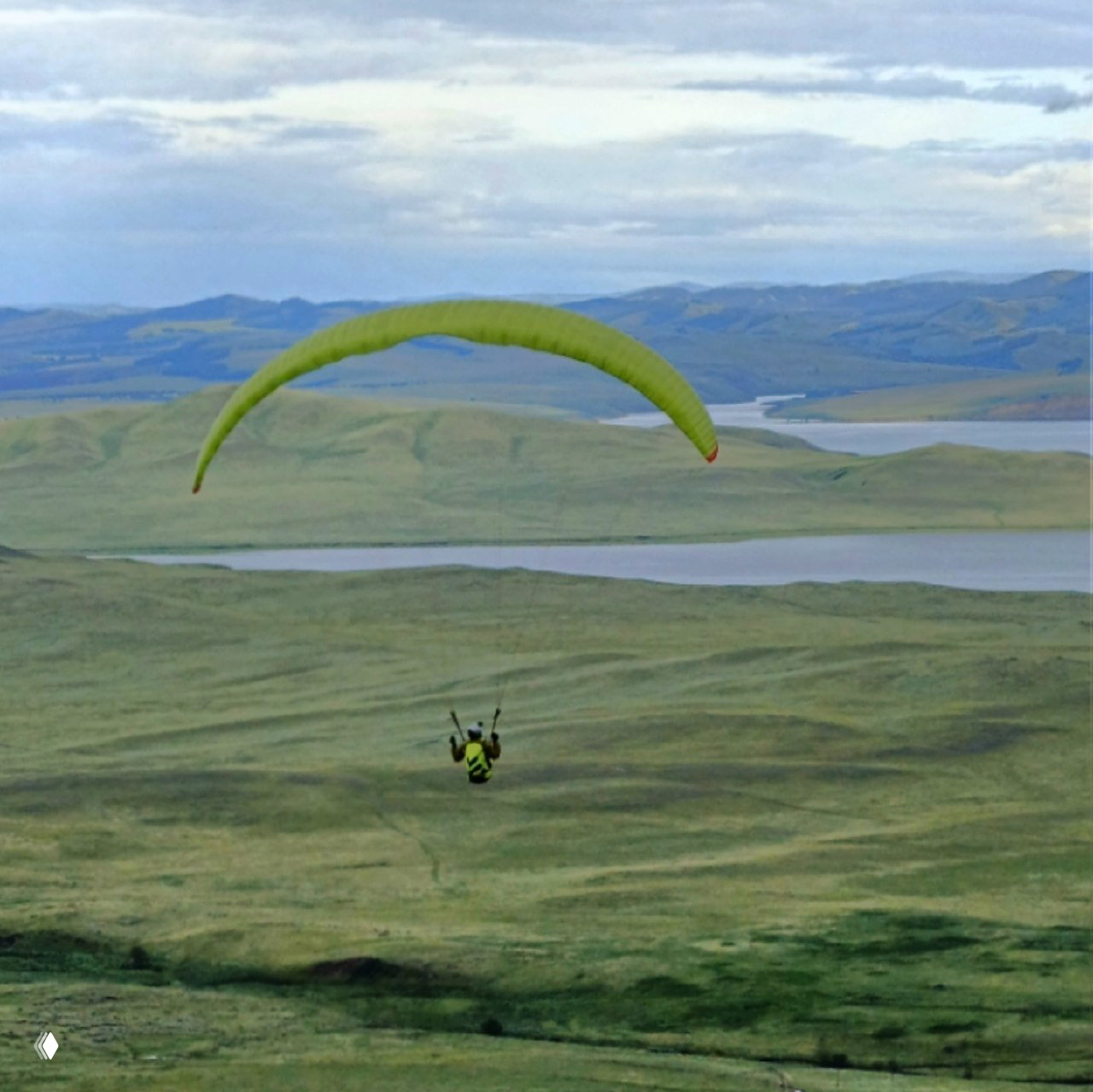 Парапланист в полёте над холмами и озёрами Хакасии: кадр подчёркивает высоту, простор и спокойствие местности в ясную погоду.