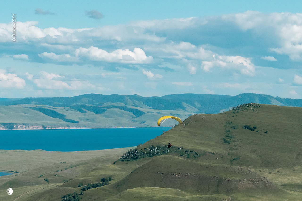 Панорамный вид склонов и озера с жёлтым парапланом на склоне — ландшафт кэмпа Лиственная и масштабный фон гор и воды.