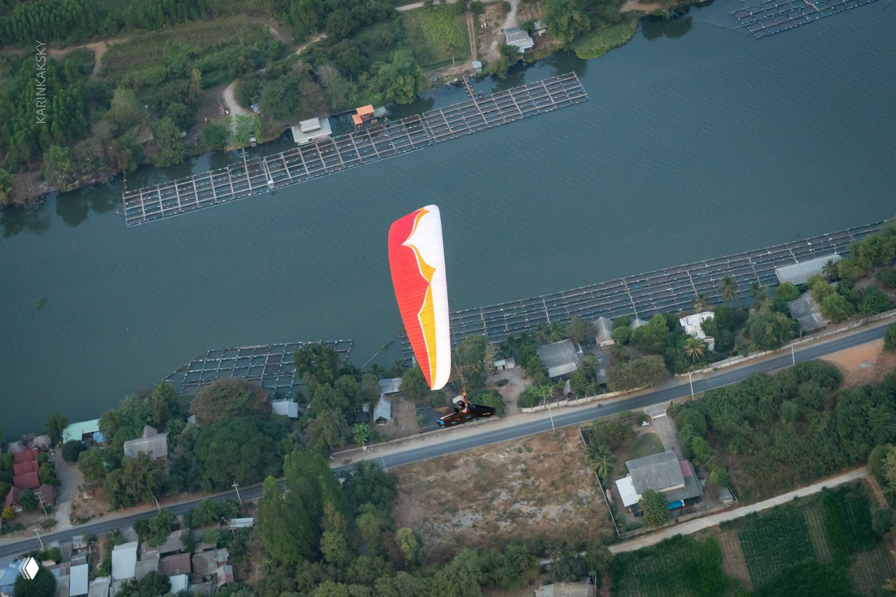Белое и красное крыло парящего пилота над водной фермой и дорогой, вид с высоты иллюстрирует посадки и маршруты вдоль побережья.