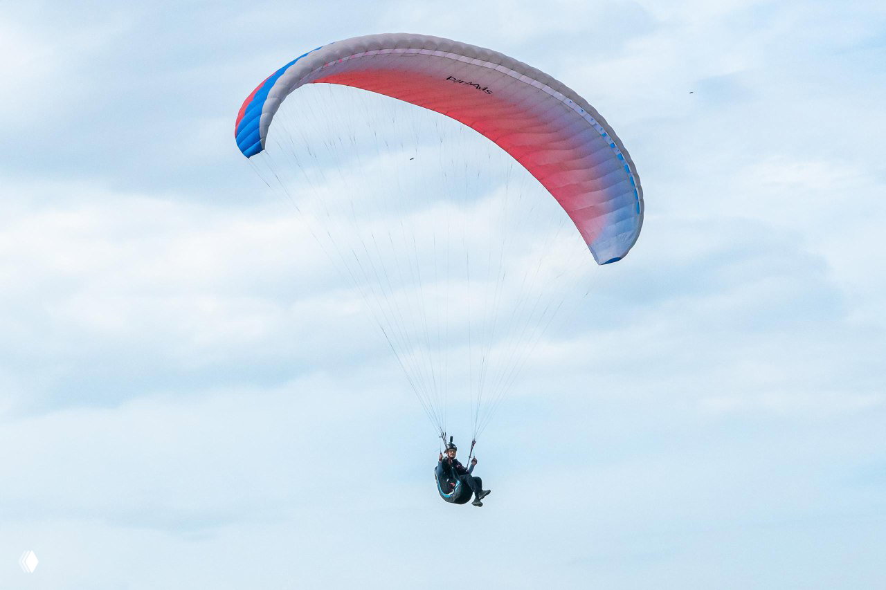 Парапланист в одиночном полёте на фоне мягкой облачности; аэродинамическая форма купола и поза пилота заметны в кадре.