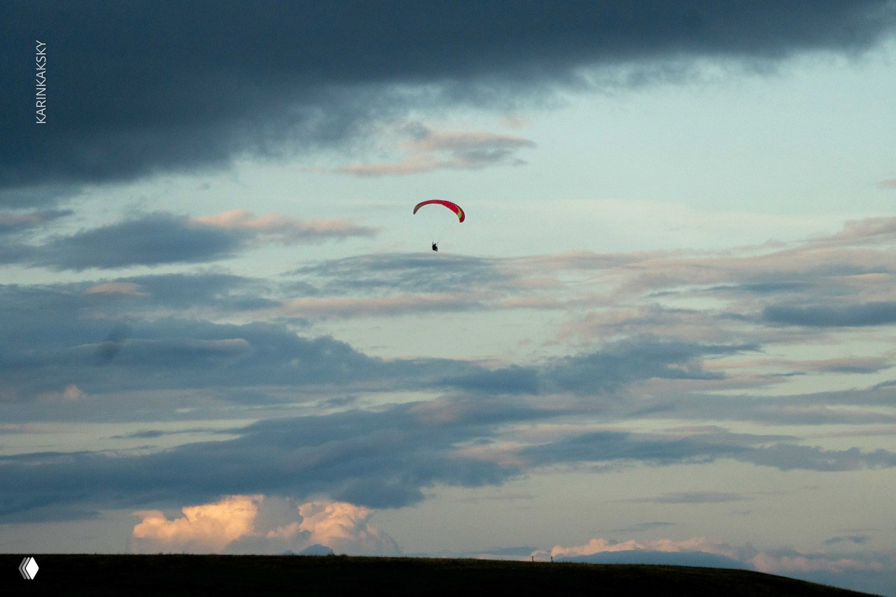Одинокий параплан в небе на фоне драматичных облаков: маленькая фигура пилота на большом пространстве неба и горизонта.