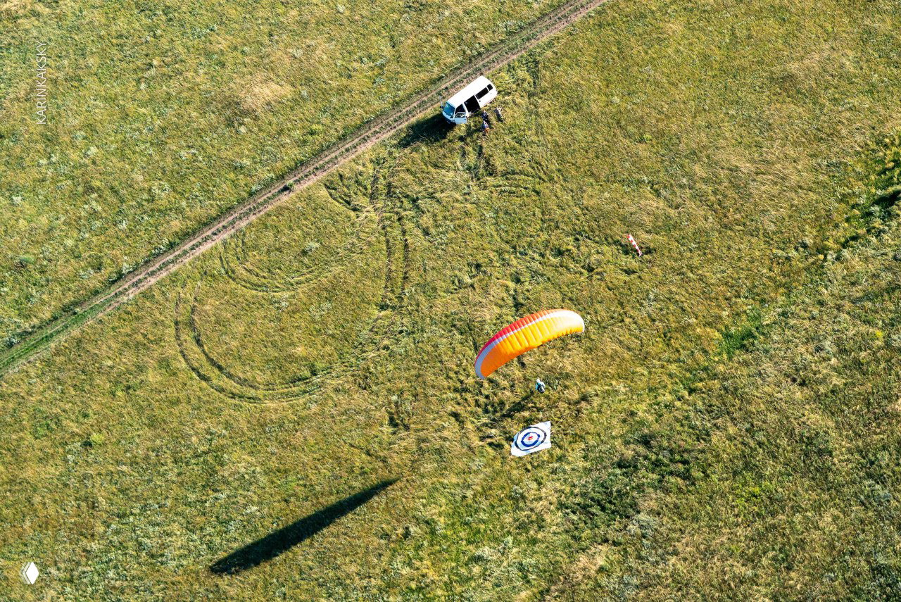 Аэровид с одного пилота и запасного автомобиля на поле: купол яркого оранжевого параплана и круг-мишень на земле.