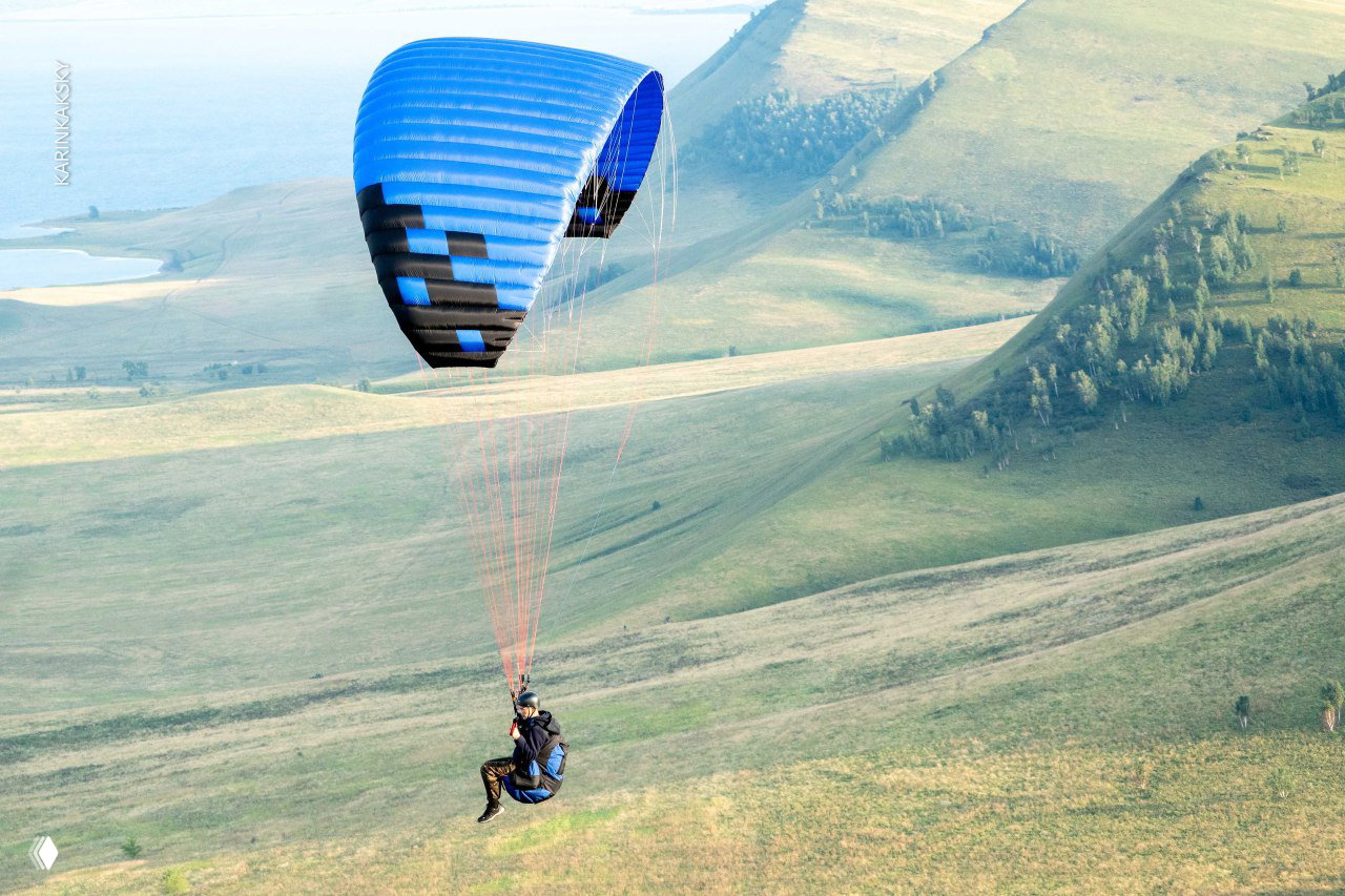 Одинокий пилот на синем крыле парящим над степными склонами; видна дуга крыла и протяжённый простор земли.
