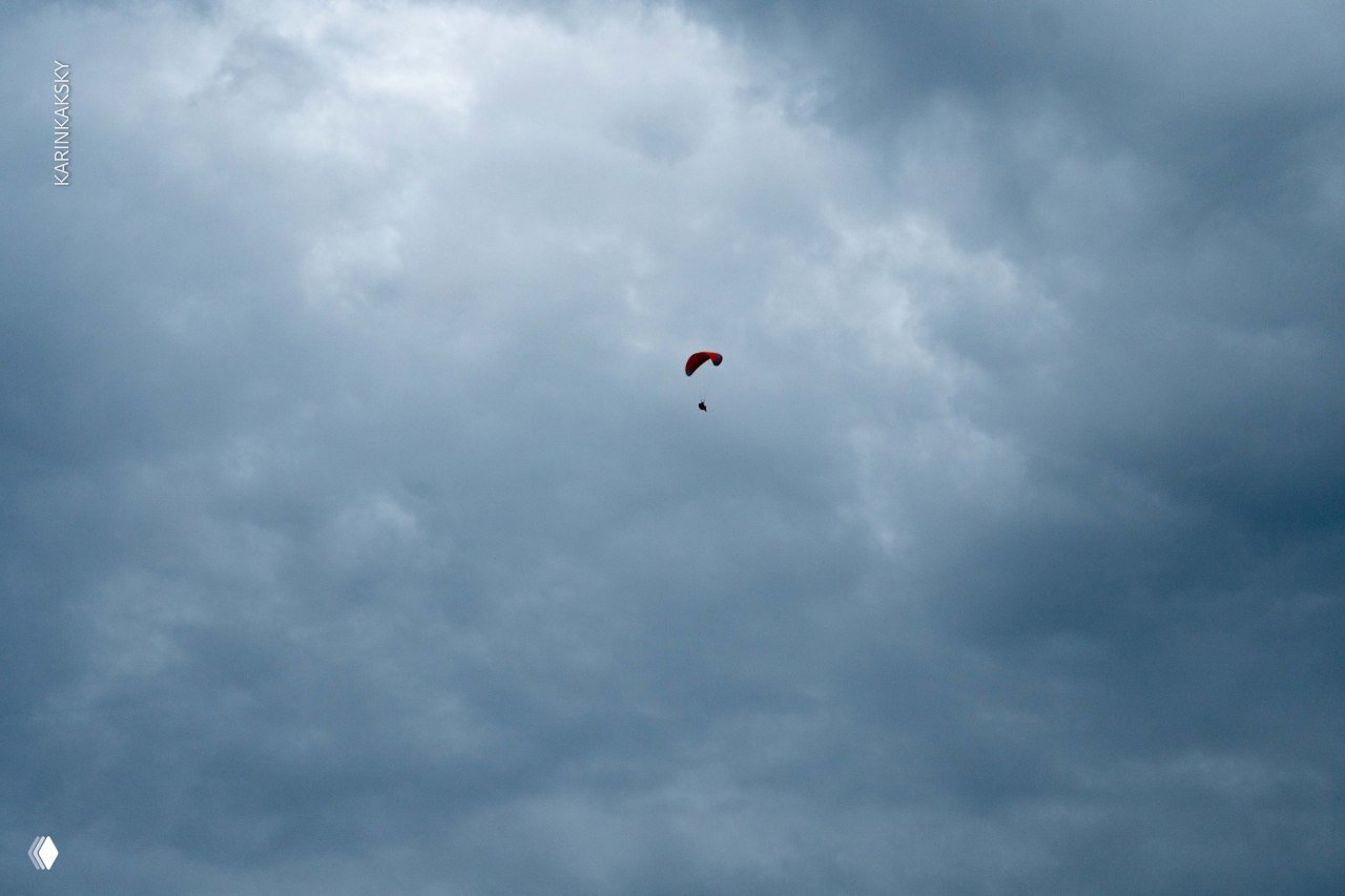 Парапланист на фоне плотного облачного неба; силуэт крыльев и пилота создают ощущение высоты и одиночества в небе.