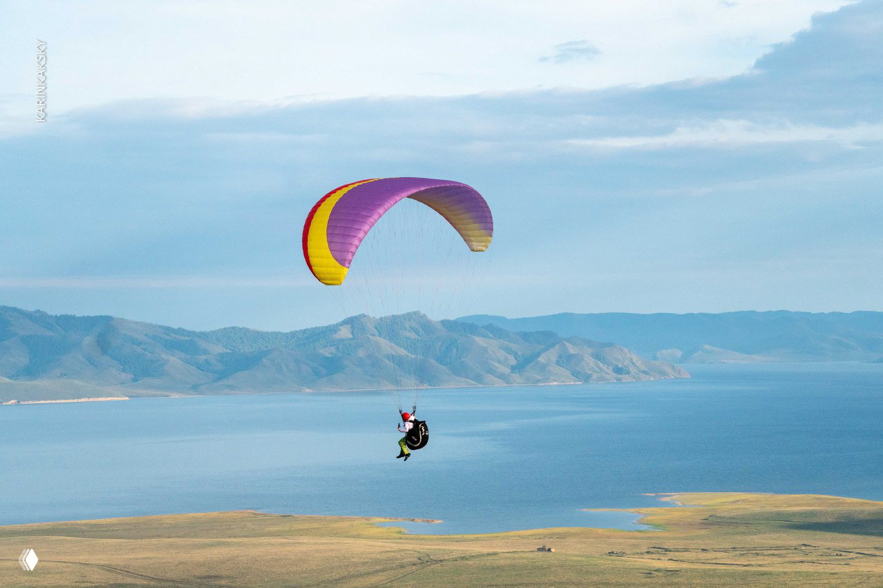 Парапланист над изгибом берега у водохранилища, широкая водная гладь и прибрежные луга видны вдали.