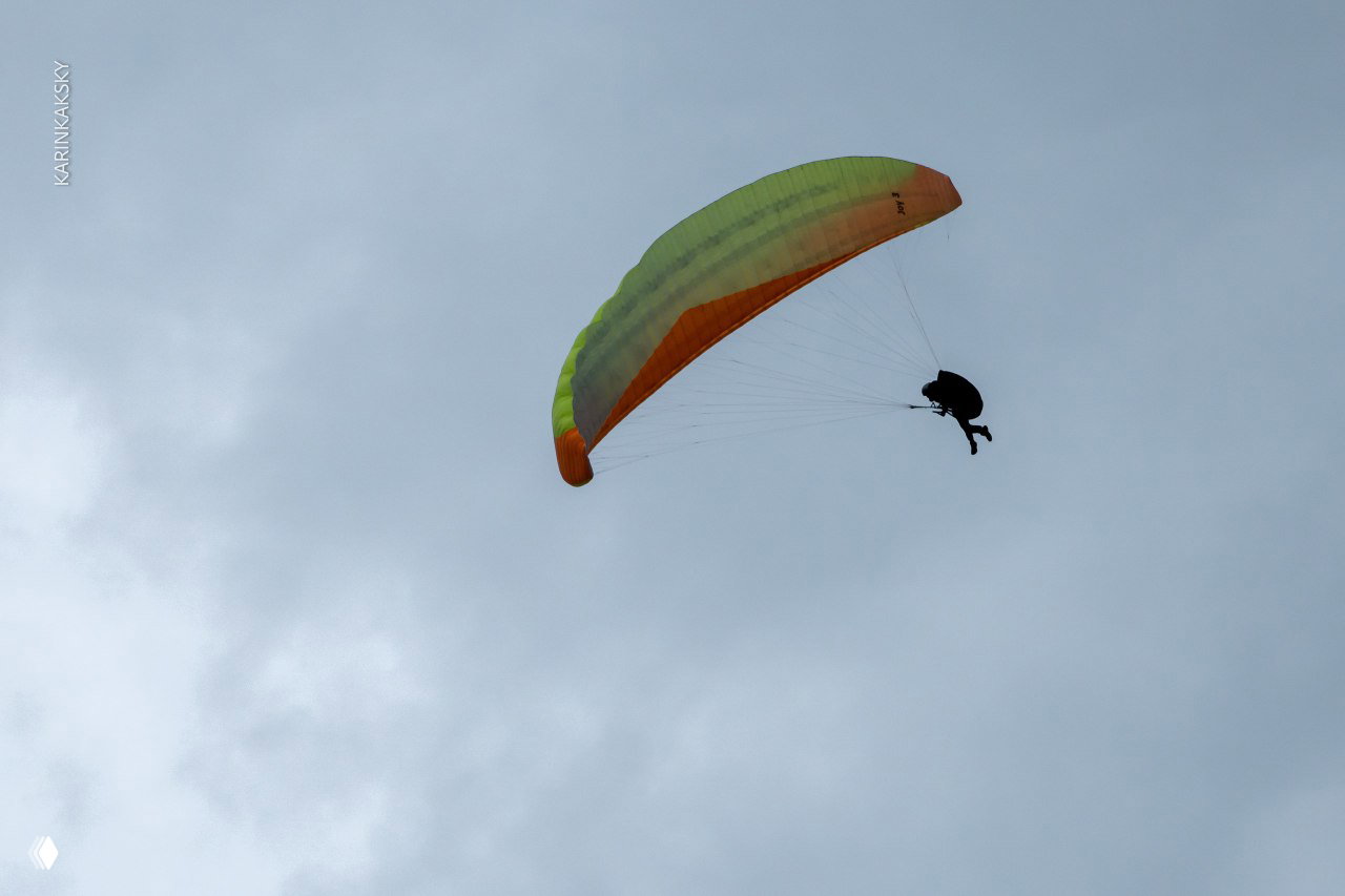 Силуэт парапланиста под светло‑серым небом, кадр подчёркивает форму крыла и воздушную свободу полёта.