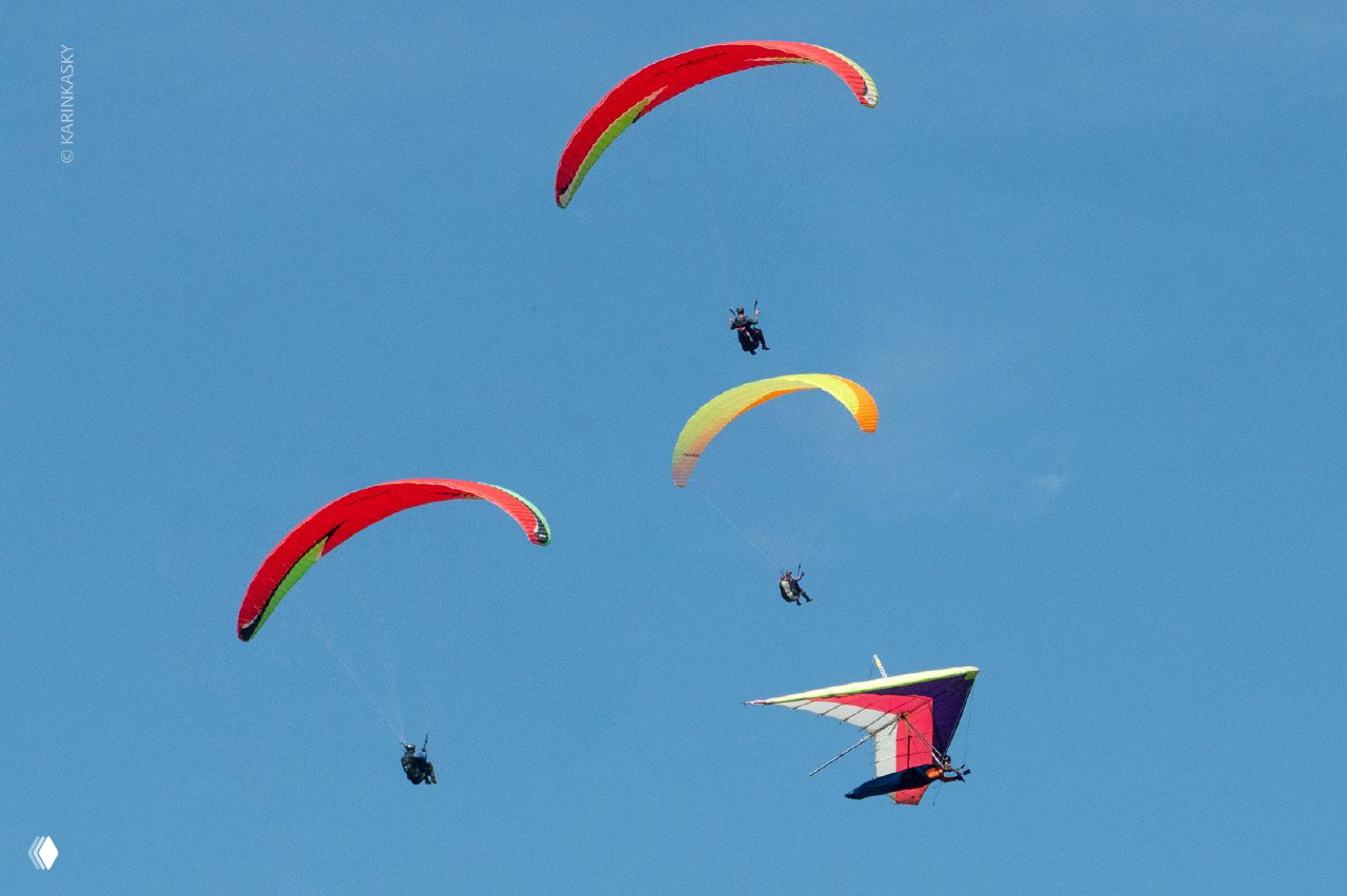 Несколько парапланов и дельтаплан на фоне чистого голубого неба: разноцветные крылья и летящие экипажи в хорошую погоду.