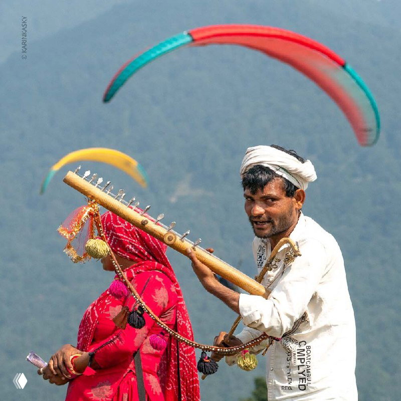 Музыкант в индийской одежде на фоне параплана: кадр сочетает культурный контекст поездки в Индию и элементы воздушного спорта.