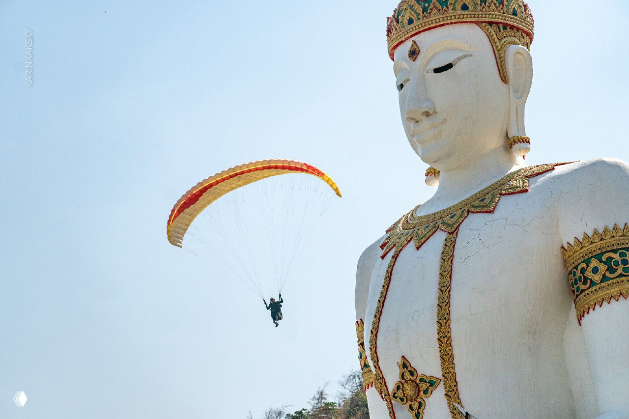 Парапланист пролетает рядом с большой белой статуей Будды — кадры из поездки в Таиланд, сочетание культуры и авиаспорта.