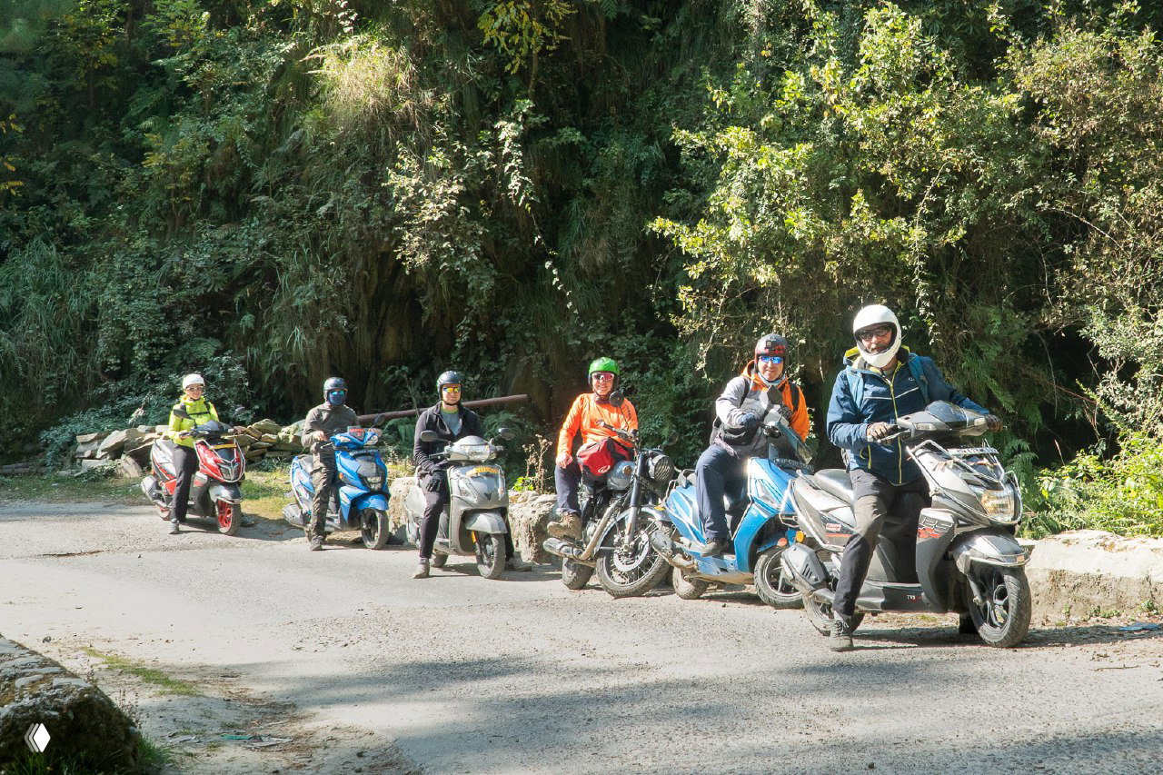 Группа пилотов на скутерах и мотоциклах на просёлочной дороге у зелёной растительности — момент перед или после выездного маршрута и подготовки.