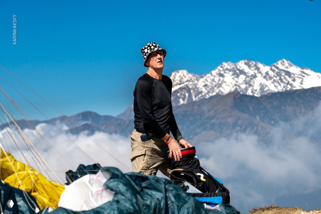 Мужчина готовит параплан к упаковке на фоне гор и ясного неба в индийских горах — кадр с бытовой сценой экипировки.