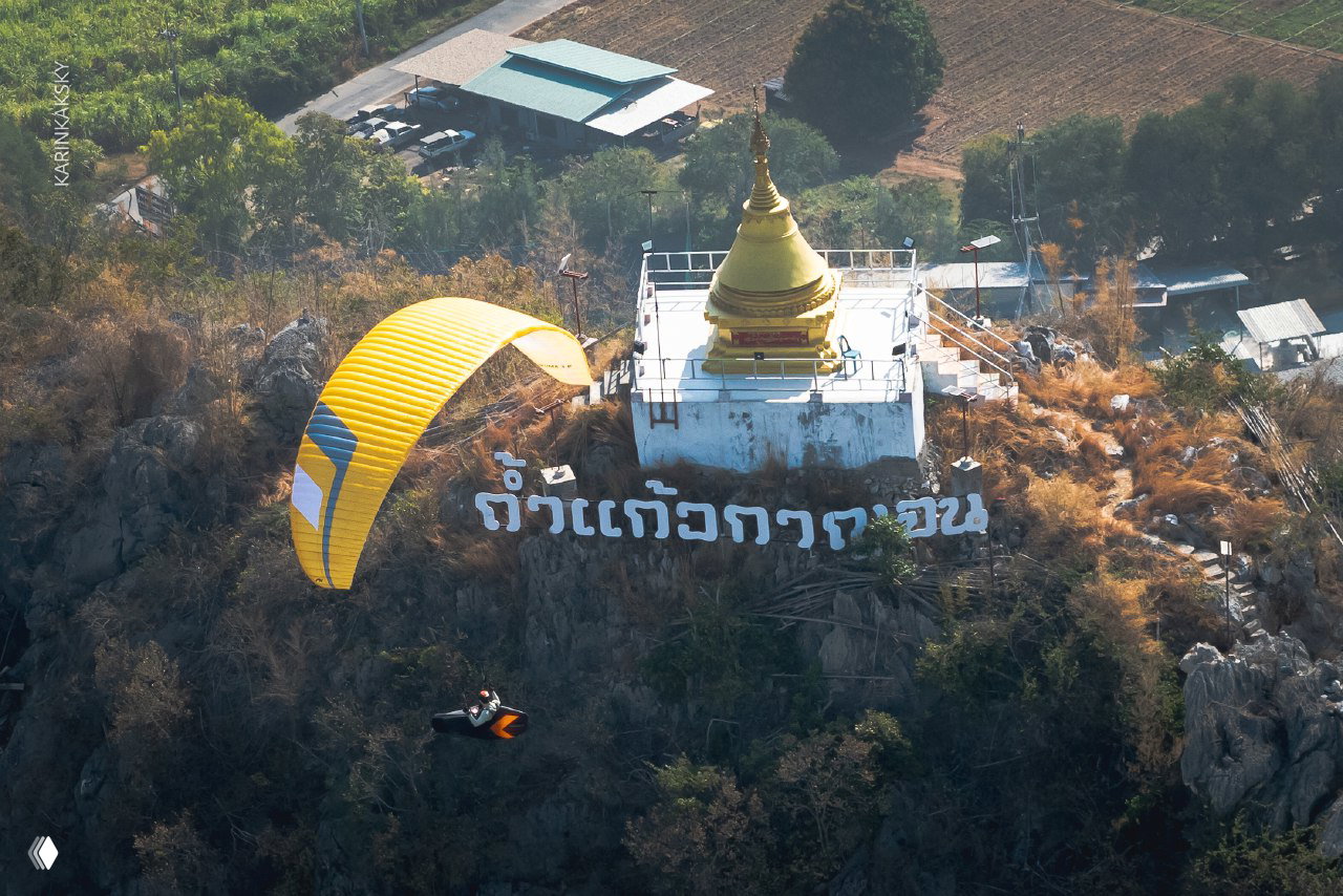 Желтый параплан рядом с золотой ступой на скале, вид с воздуха на стартовую площадку и холмы — крупный план полета.