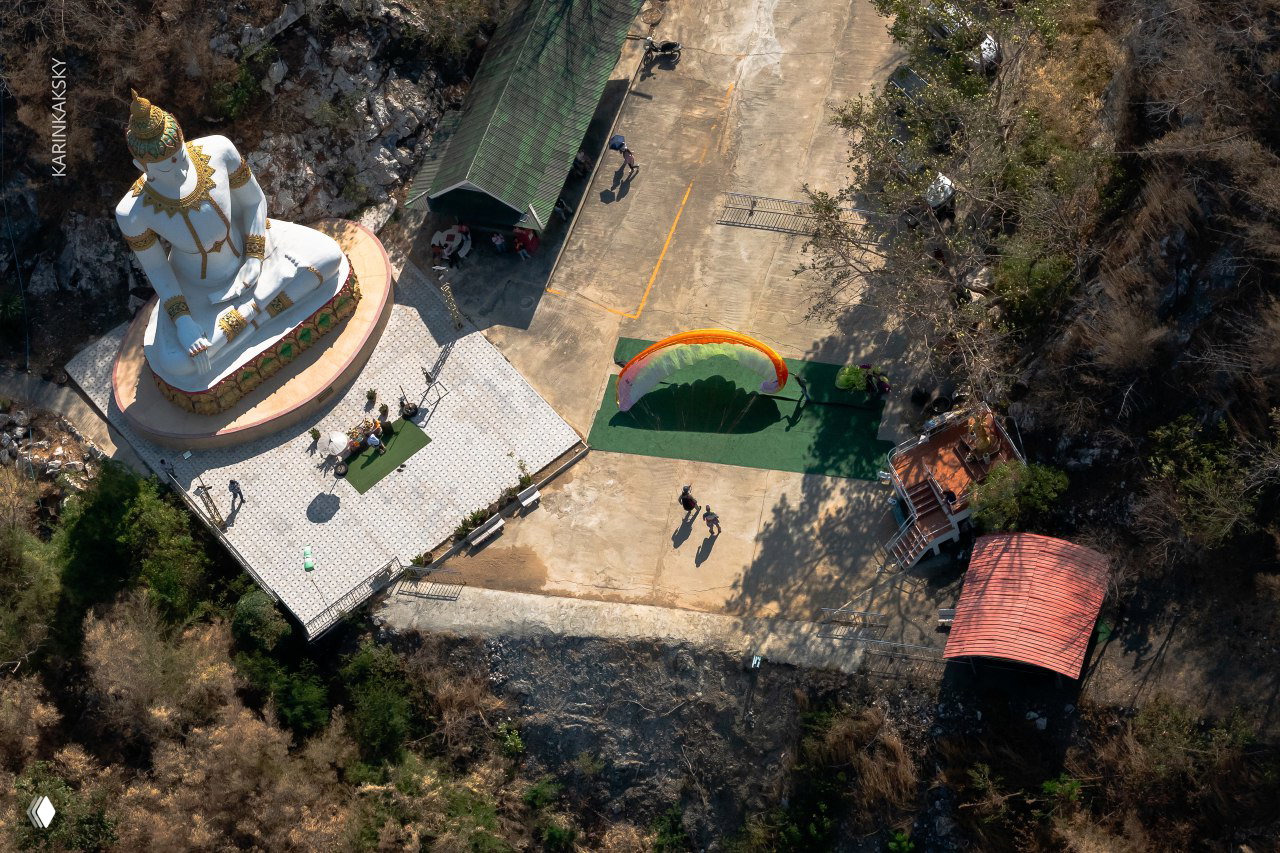 Аэрофото с высоты: белая статуя Будды, параплан на площадке и люди на старте — вид сверху на тренировочную зону.