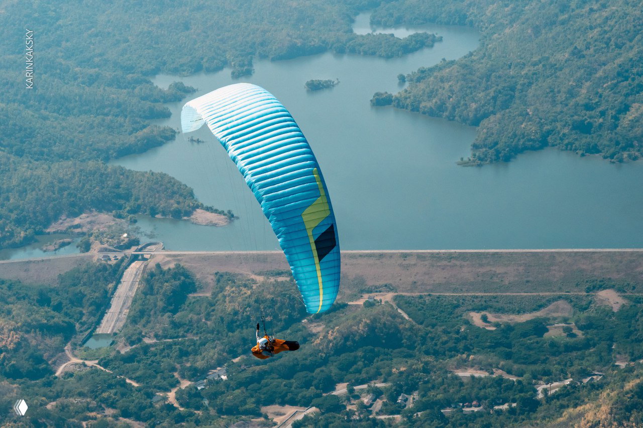 Голубой параплан в полёте над водохранилищем и зелёными холмами, кадр с высоты подчёркивает маршрут и перспективу полёта.