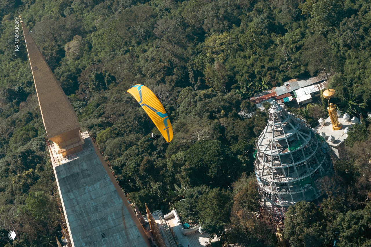 Жёлтый параплан в облаках над храмовыми комплексами и строящимся зданием пагоды — аэросъёмка стартов и ландшафта.